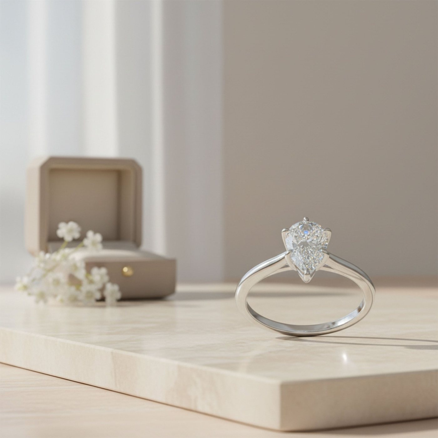 A pear-shaped ring beside a jewelry box and flowers